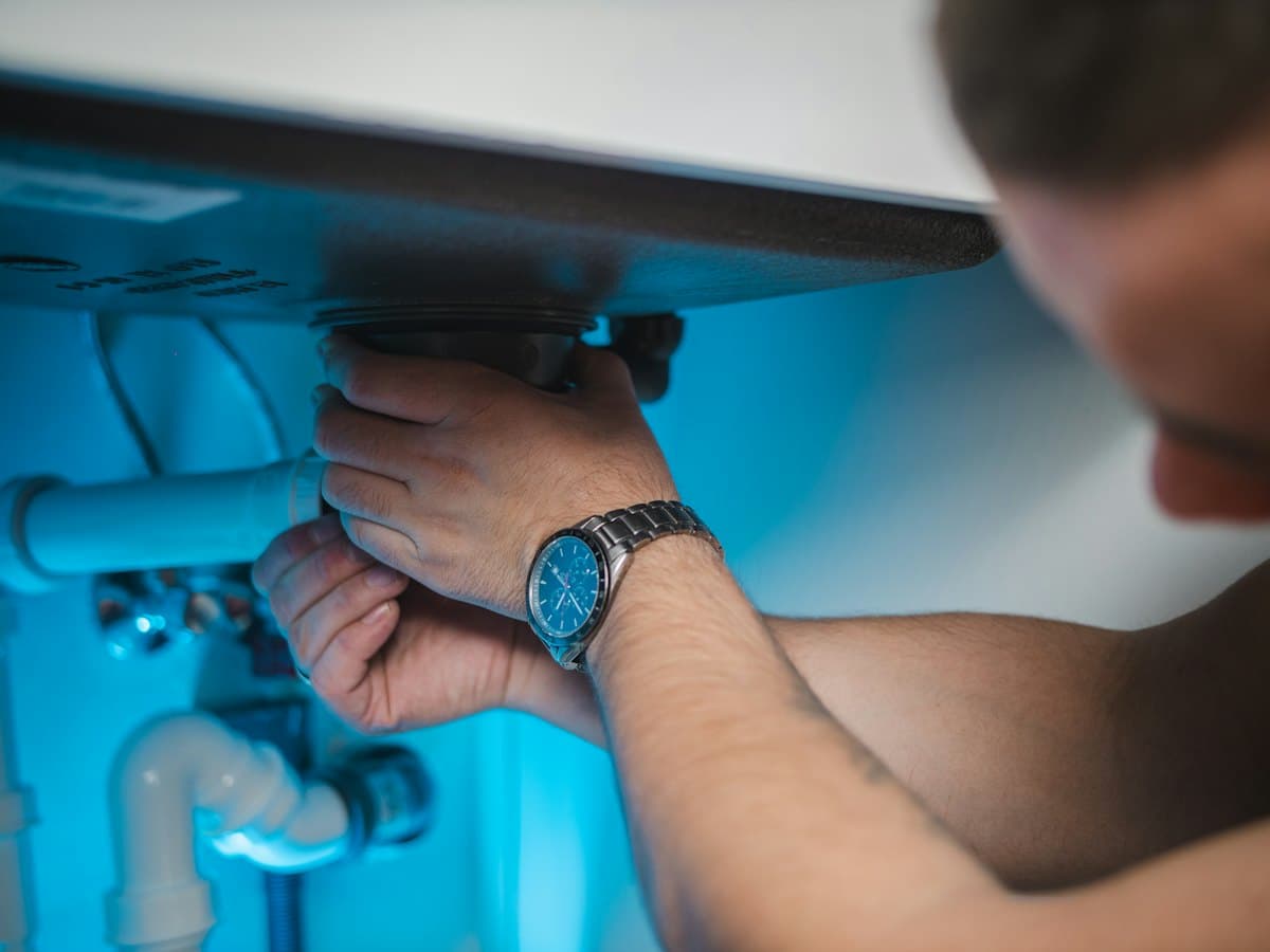 A plumber fixing pipework under a sink